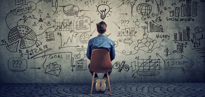 A man sitting on a chair, facing a wall covered with various business and innovation sketches and diagrams.